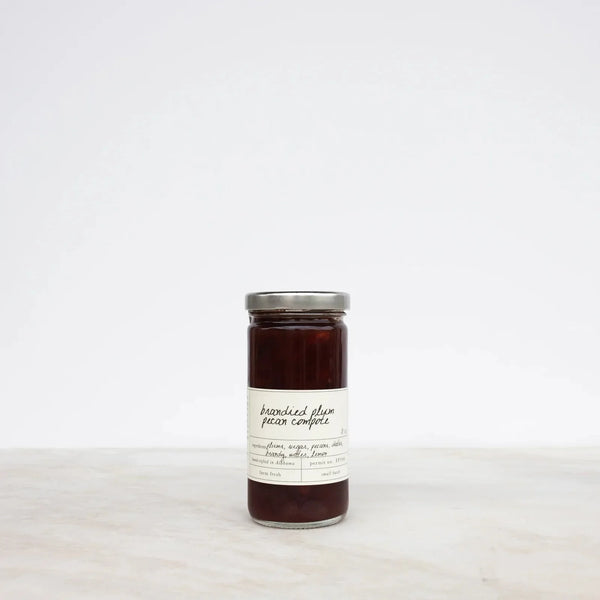 Jar of brandied plum and pecan preserves on a marble table top