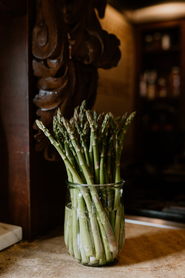 A bundle of Asparagus in a glass jar on a kitchen countertop