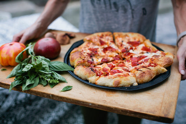A wooden cutting board full of pizza, basil, and heirloom tomatoes