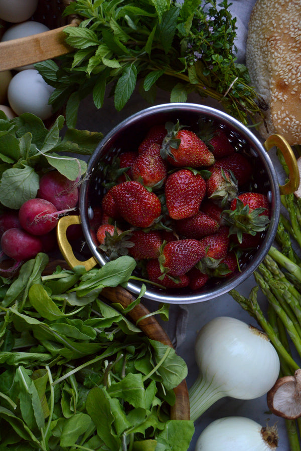 An array of fruits and vegetables on a linen cloth including strawberries, asparagus, and shiitake mushrooms