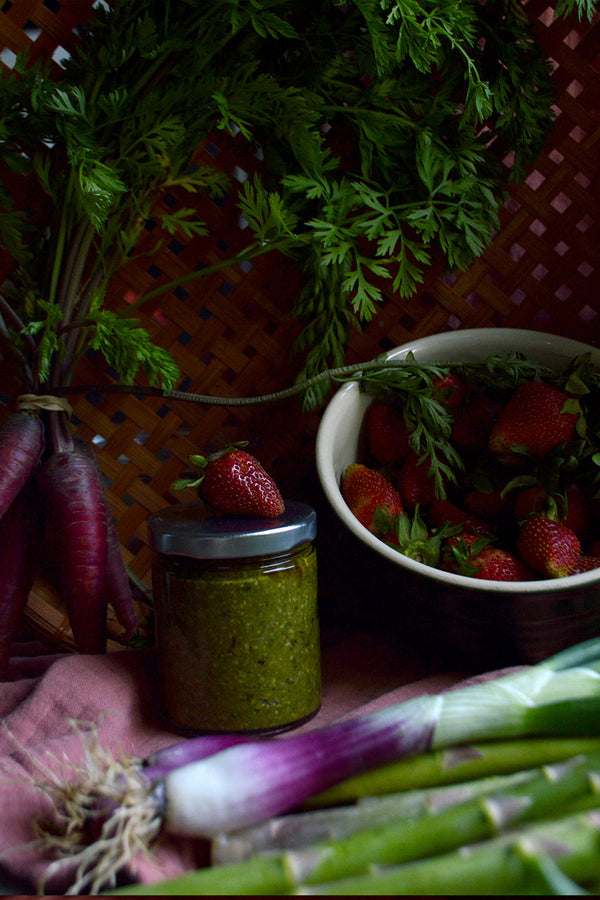 A dark moody scene of ramp pesto, fresh strawberries, red onions, and carrots
