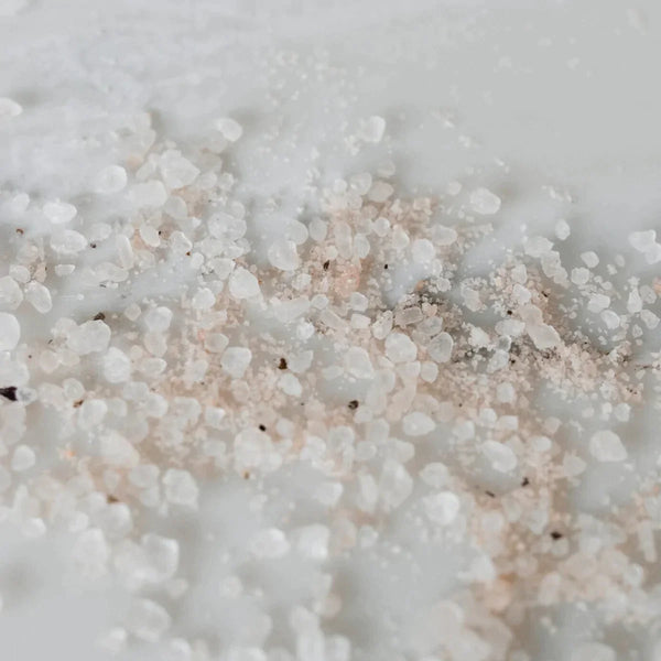Rose-colored pink bath salts scattered on a marble tabletop
