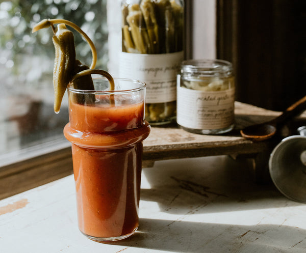Glass of bloody mary mix cocktail with pickled okra and pickled garlic scapes