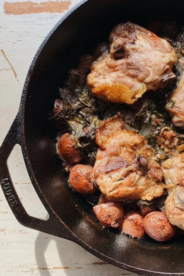 A roasting pan filled with chicken thighs and spring vegetables