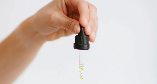 A hand releasing a few drops from the dropper full of our vitamin e nourishing oil onto their other hand
