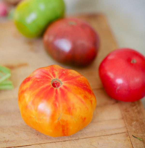 Heirloom tomatoes in a variety of reds, oranges, and greens on a cutting board