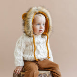 Child wearing the cream Fisherman Sweater and a lion bonnet, Stone Hollow Farmstead