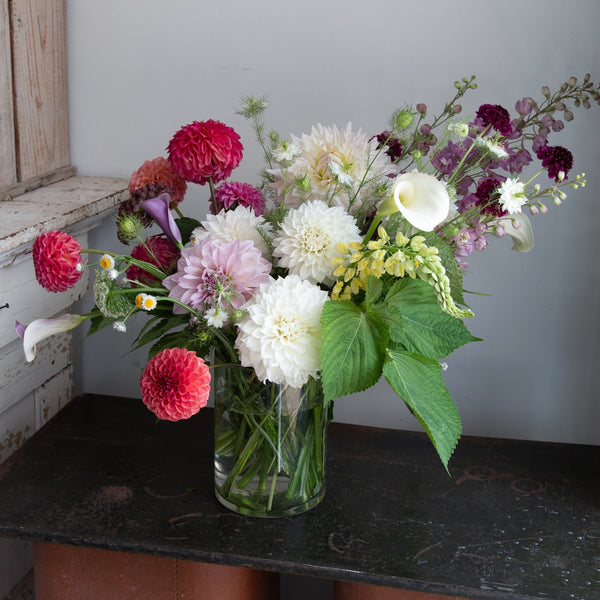 Bouquet of Dahlias in a clear vase on a dark surface with a light gray wall background