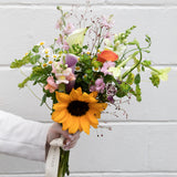 Bouquet of flowers with a sunflower held by a person against a light gray background